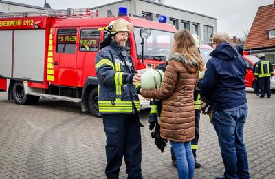 Zwei Feuerwehrmänner geben einer Frau und einem Mann Feuerwehrkleidung.